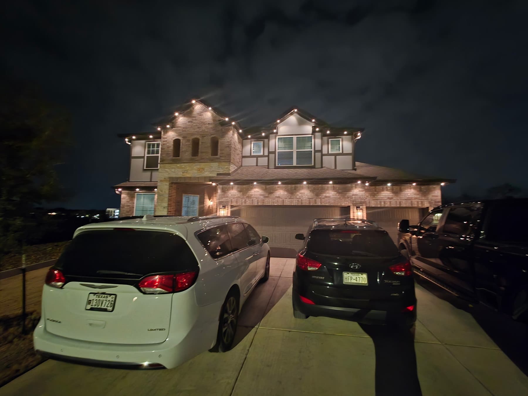 Customer-supplied LIT365 installation: a home's central facade and driveway with vehicles, lit by warm-white permanent roofline lighting