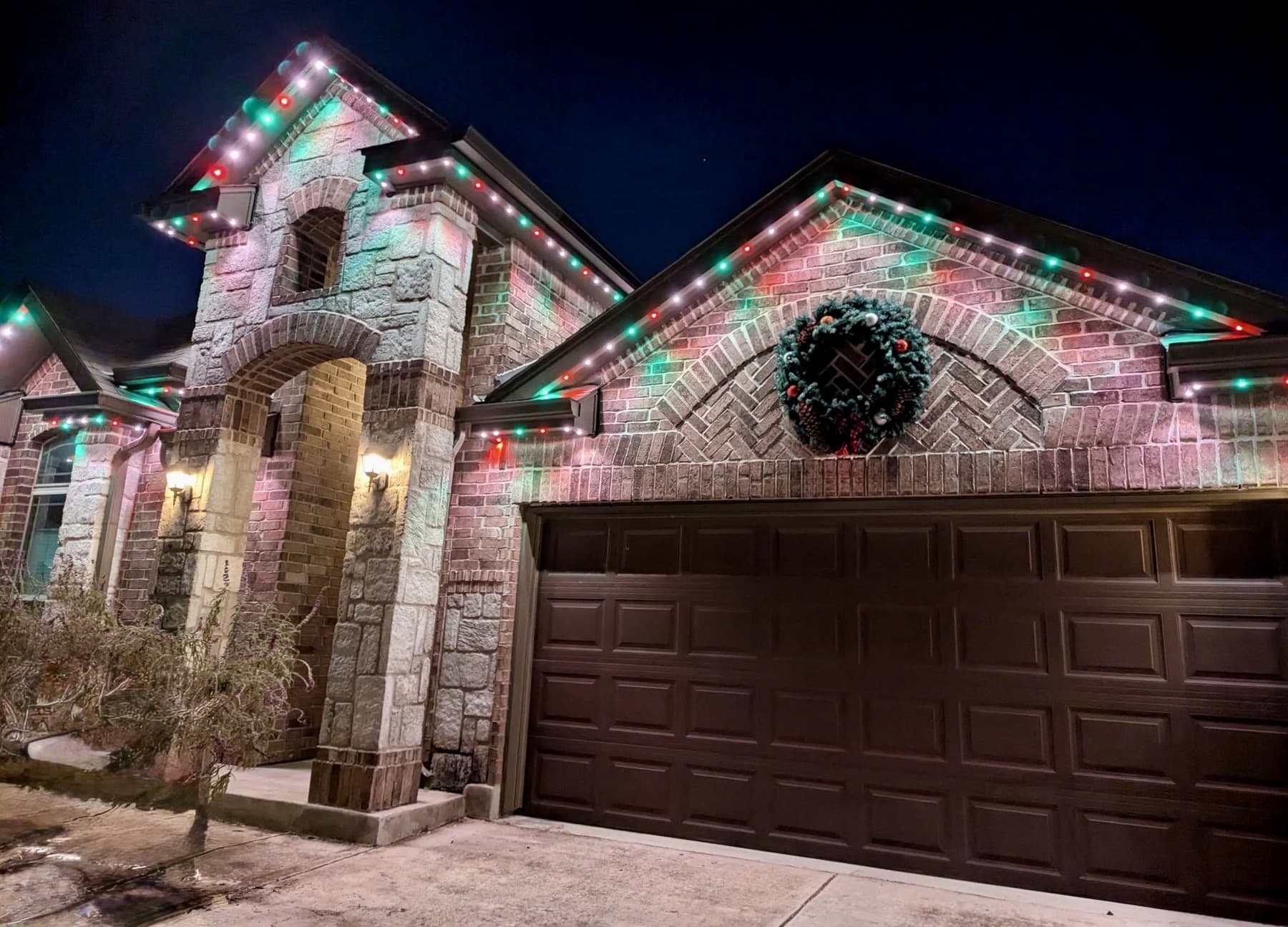 Customer-supplied LIT365 installation: a patio and tree-shaded facade under a multicolor permanent-lighting scene at night