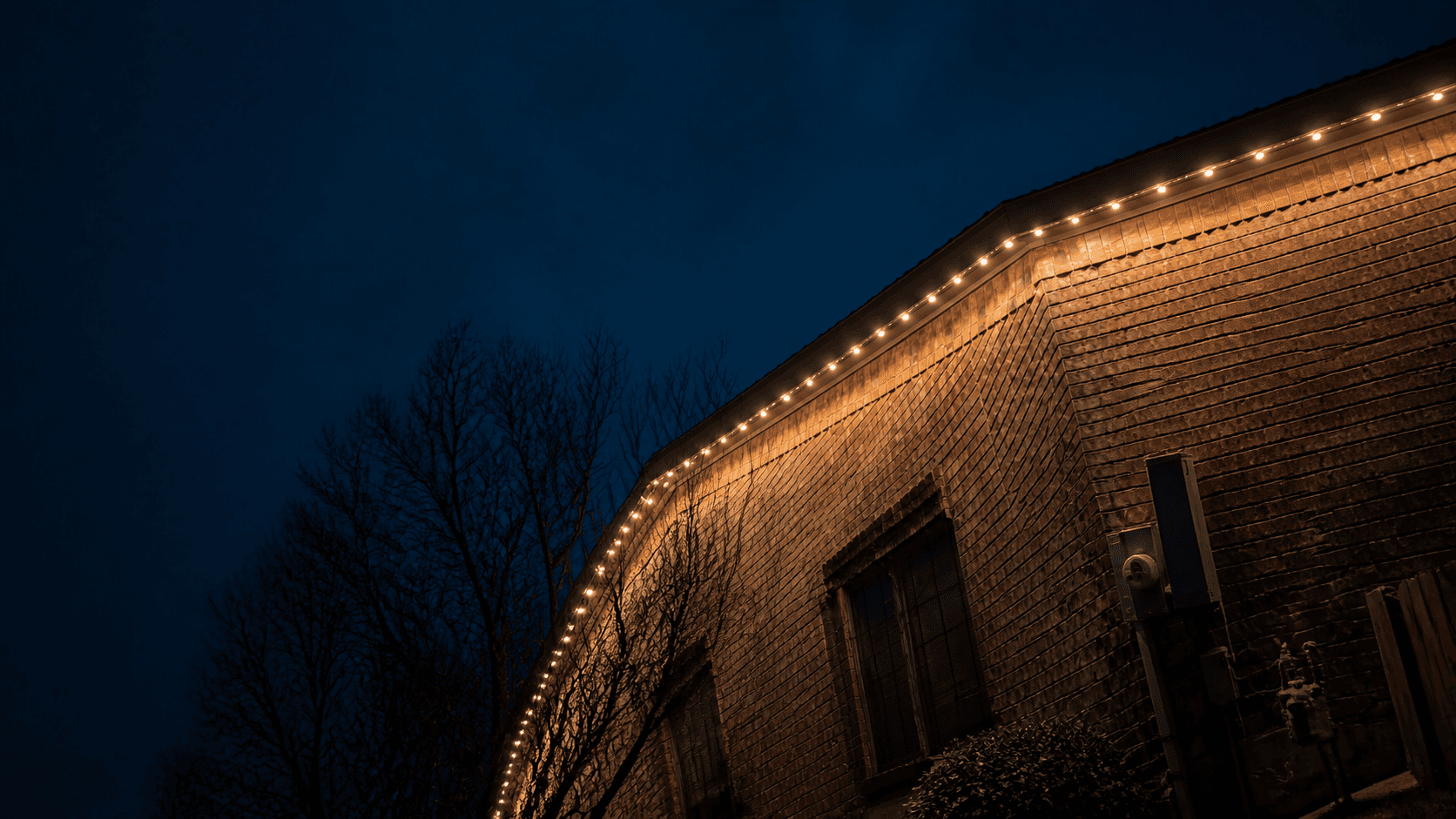 Customer-supplied LIT365 installation detail: warm permanent lighting follows a brick eave where the roofline and gutter meet at night