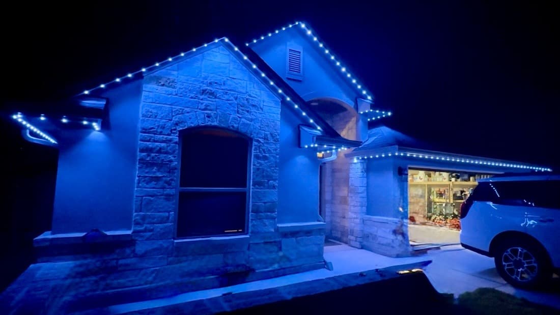 Customer-supplied LIT365 installation: front gables, lit eaves, and garage of a home under cool blue permanent lighting at night