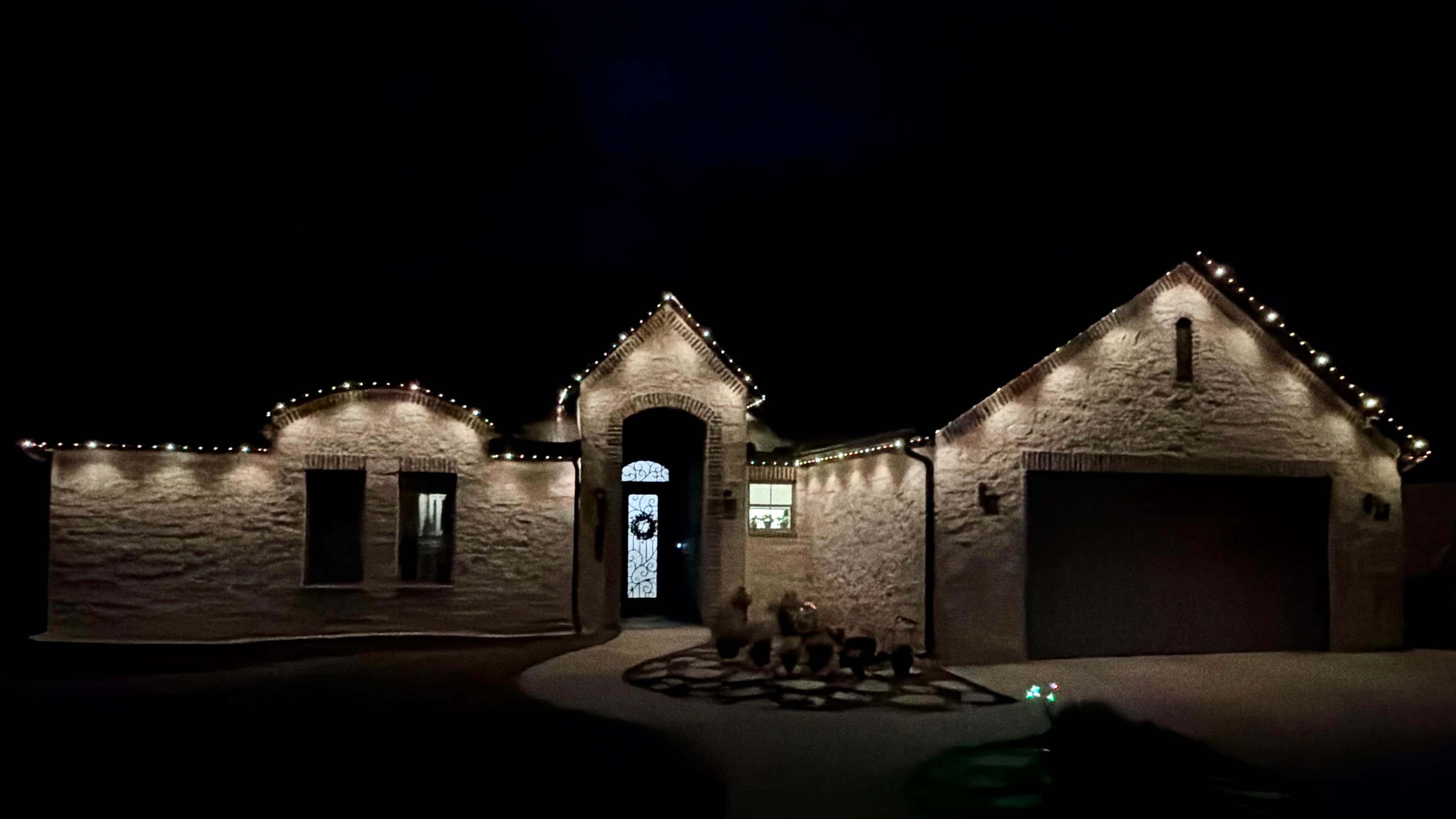 Customer-supplied LIT365 installation: a stone home's complete facade and central entrance under warm-white permanent roofline lighting at night