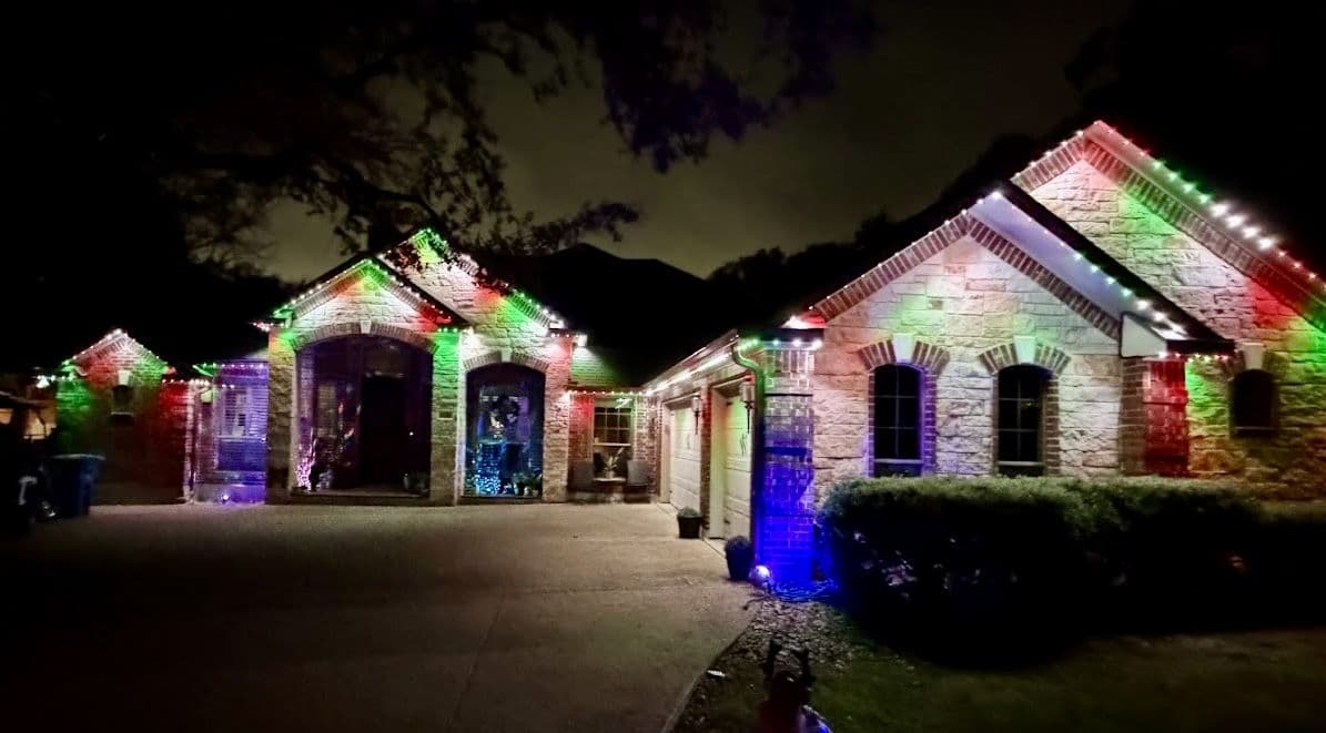Residential home with red, green, and white permanent roofline lighting at night