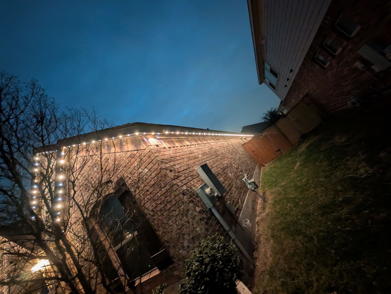 Detail of warm white permanent lighting along a brick roofline at dusk